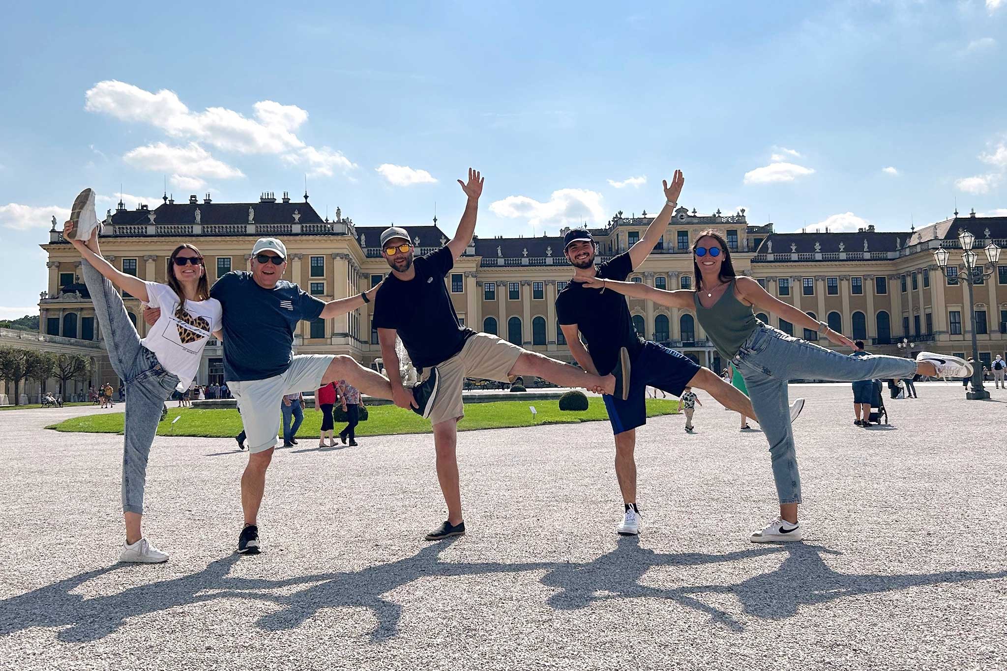 Vier Personen aus der Kanzlei springen lachend vor einem historischen Schloss und posieren mit ausgestreckten Armen und Beinen.
