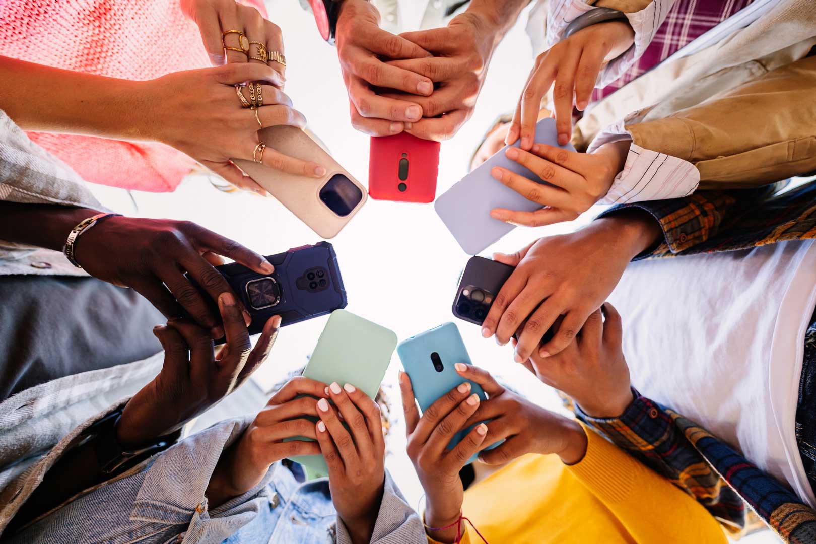Mehrere Hände halten farbige Smartphones in einem Kreis, von unten fotografiert.