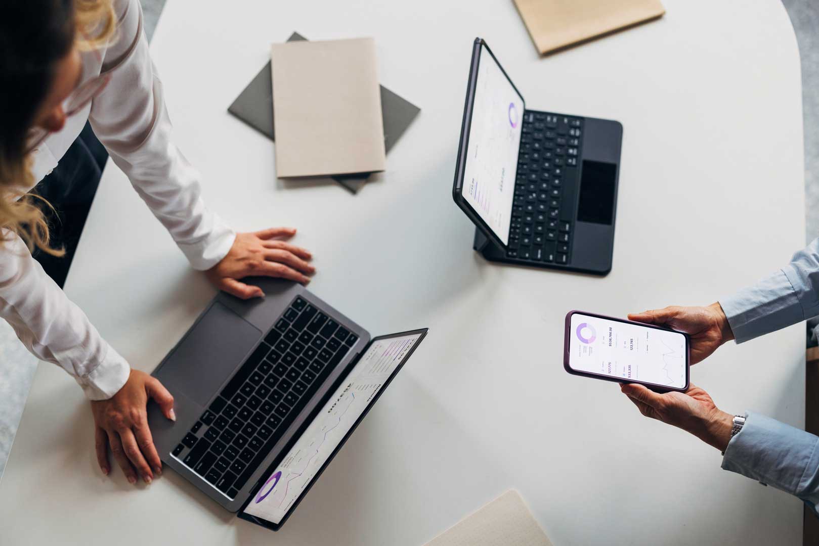 Menschen beugen sich über Laptops und halten Smartphone mit Diagrammen.